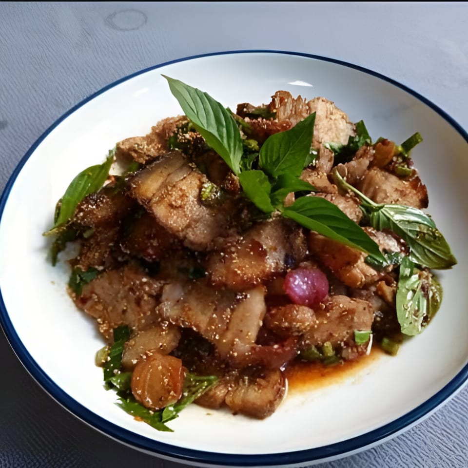 Thai pork dish with fresh basil, red onions, and green herbs on a white plate.