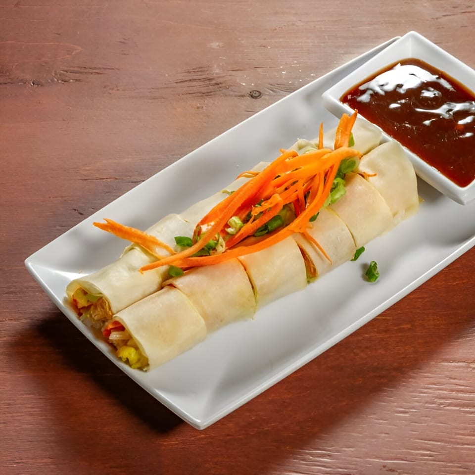 Fresh spring rolls with shredded carrots and green onions, served with a side of dark dipping sauce.
