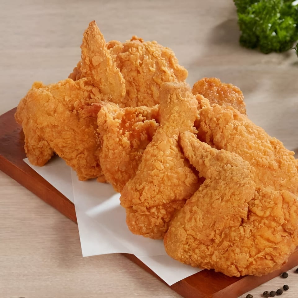 Crispy fried chicken pieces, golden brown and piled on a wooden board with white paper.