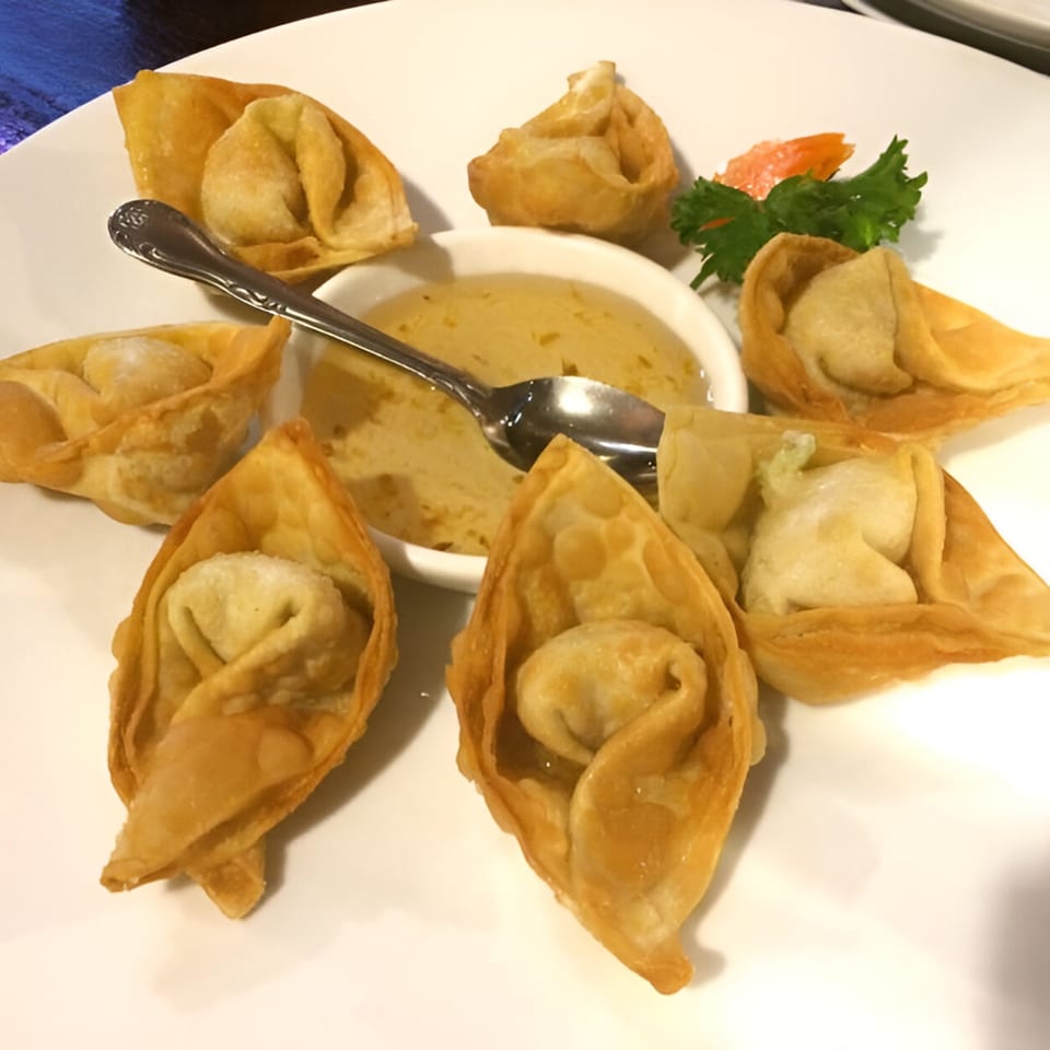 Golden-fried wontons arranged around a small bowl of dipping sauce with a spoon on a white plate.