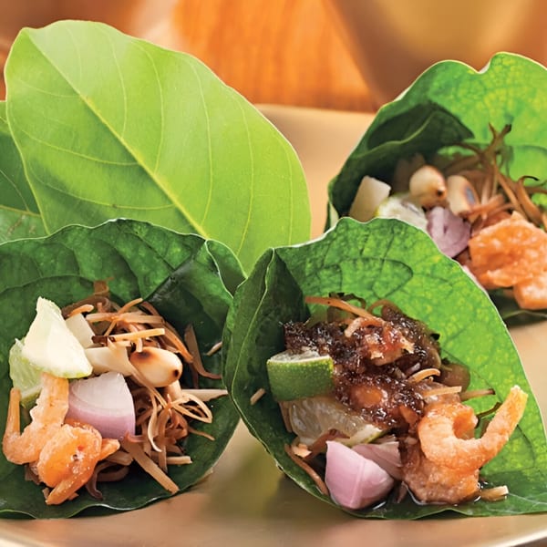 Three Thai Miang Kham appetizers, with shrimp, lime, onions, and sauce wrapped in green leaves.